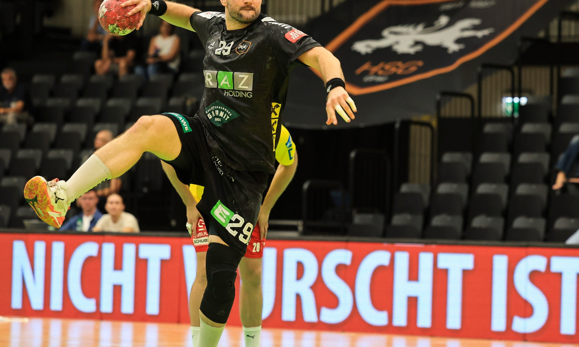 Handballspieler mit Ball in Sprungaktion, Nummer 29, in Sporthalle